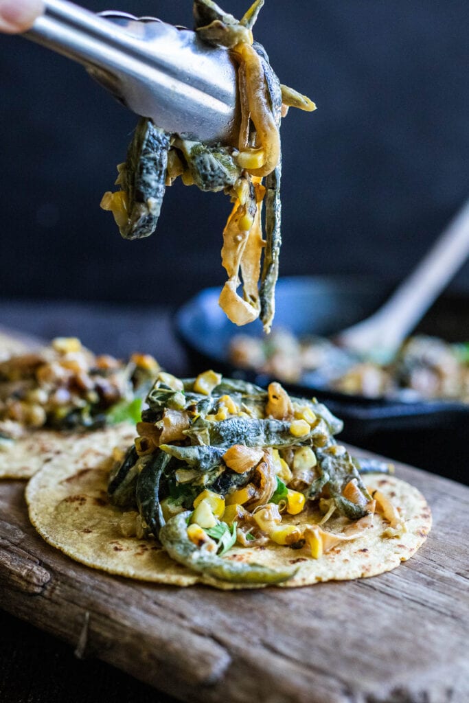 tongs picking up rajas tacos filling to place into a corn tortilla.