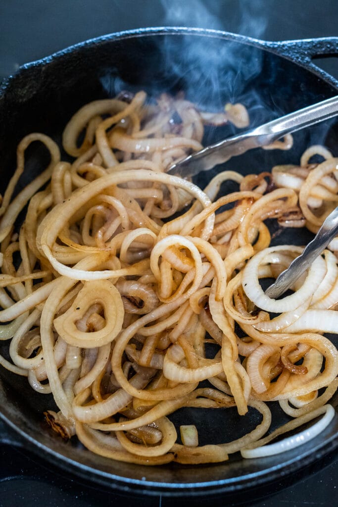 sautéeing onions with tongs in cast iron skillet.