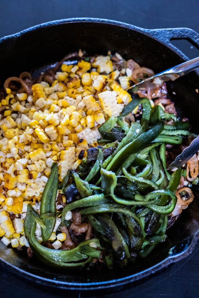 making rajas tacos- adding the corn and peppers to the cast iron skillet.