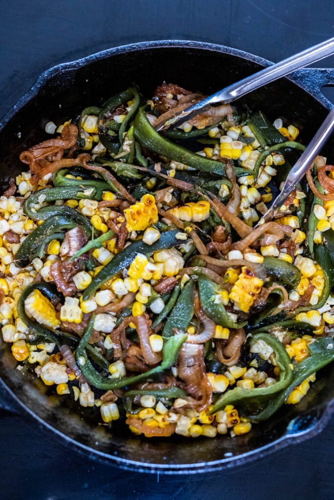stirring the rajas filling with tongs in a cast iron skillet.