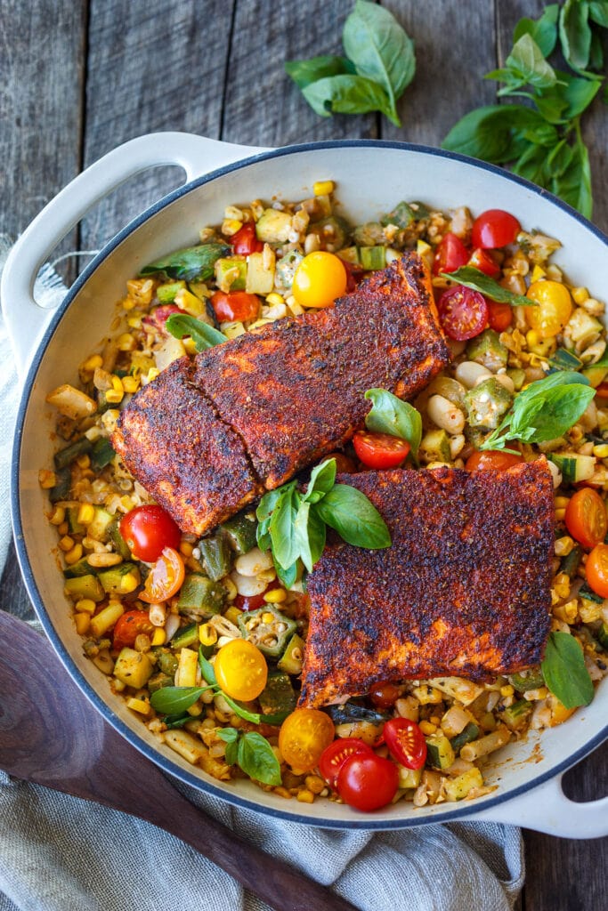 traditional succotash in a dutch oven with cherry tomatoes, blackened salmon and fresh basil.