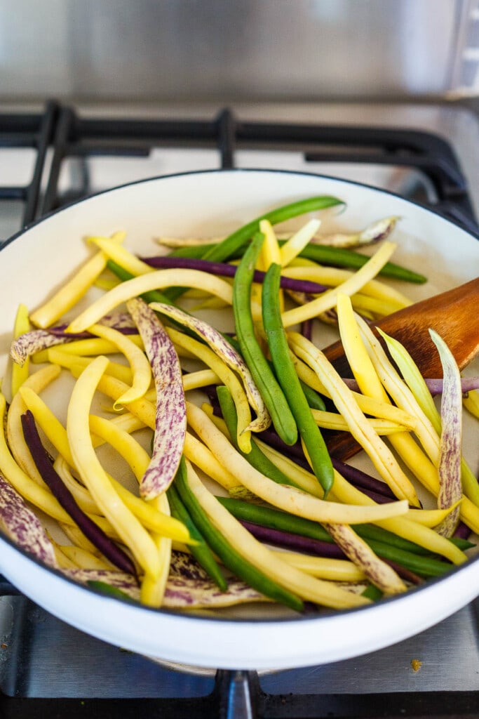 Dry frying fresh green beans in a white ceramic brasier.