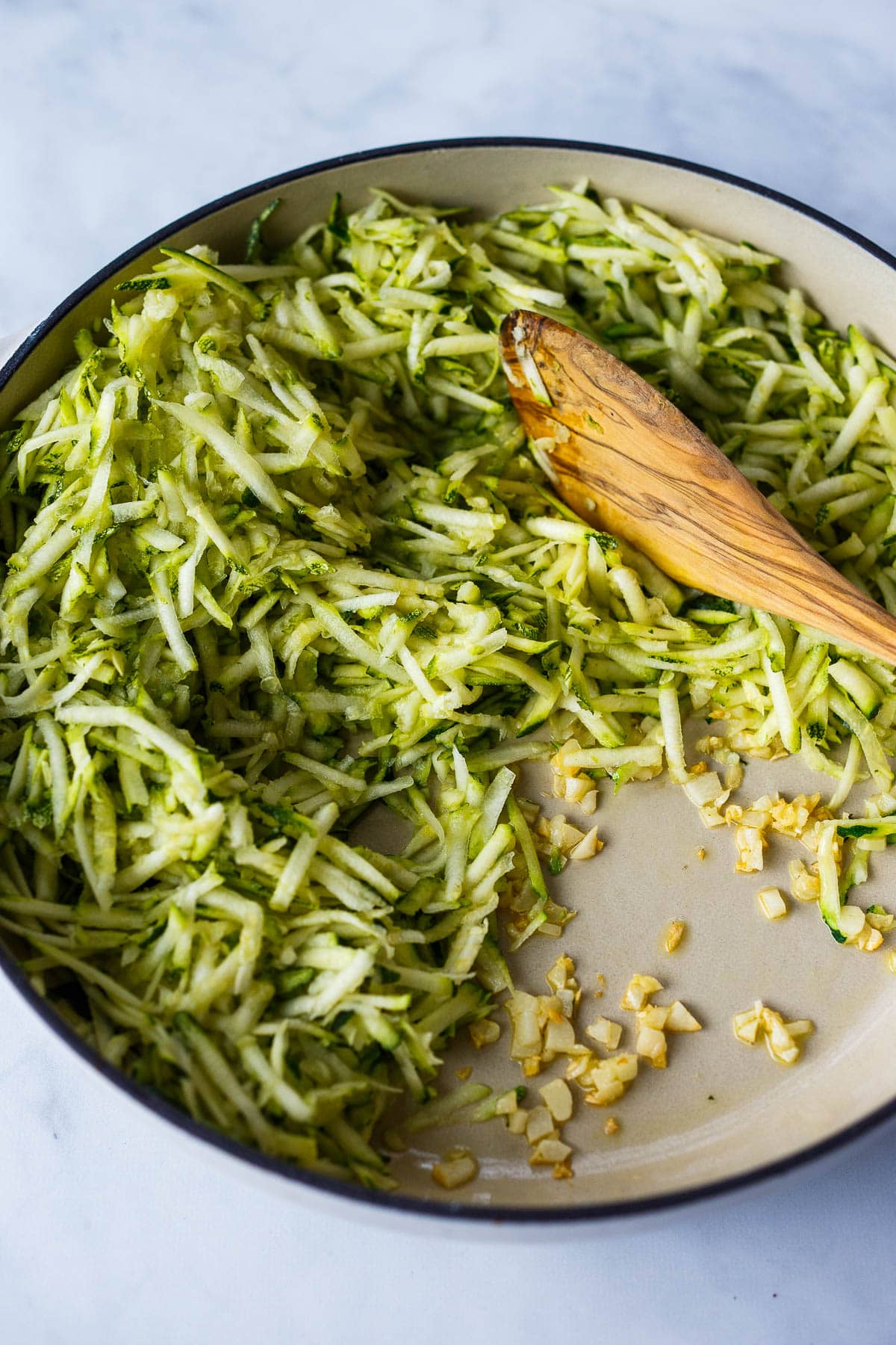 Sautéing garlic and grated zucchini with a wooden spoon in a cream brasier.