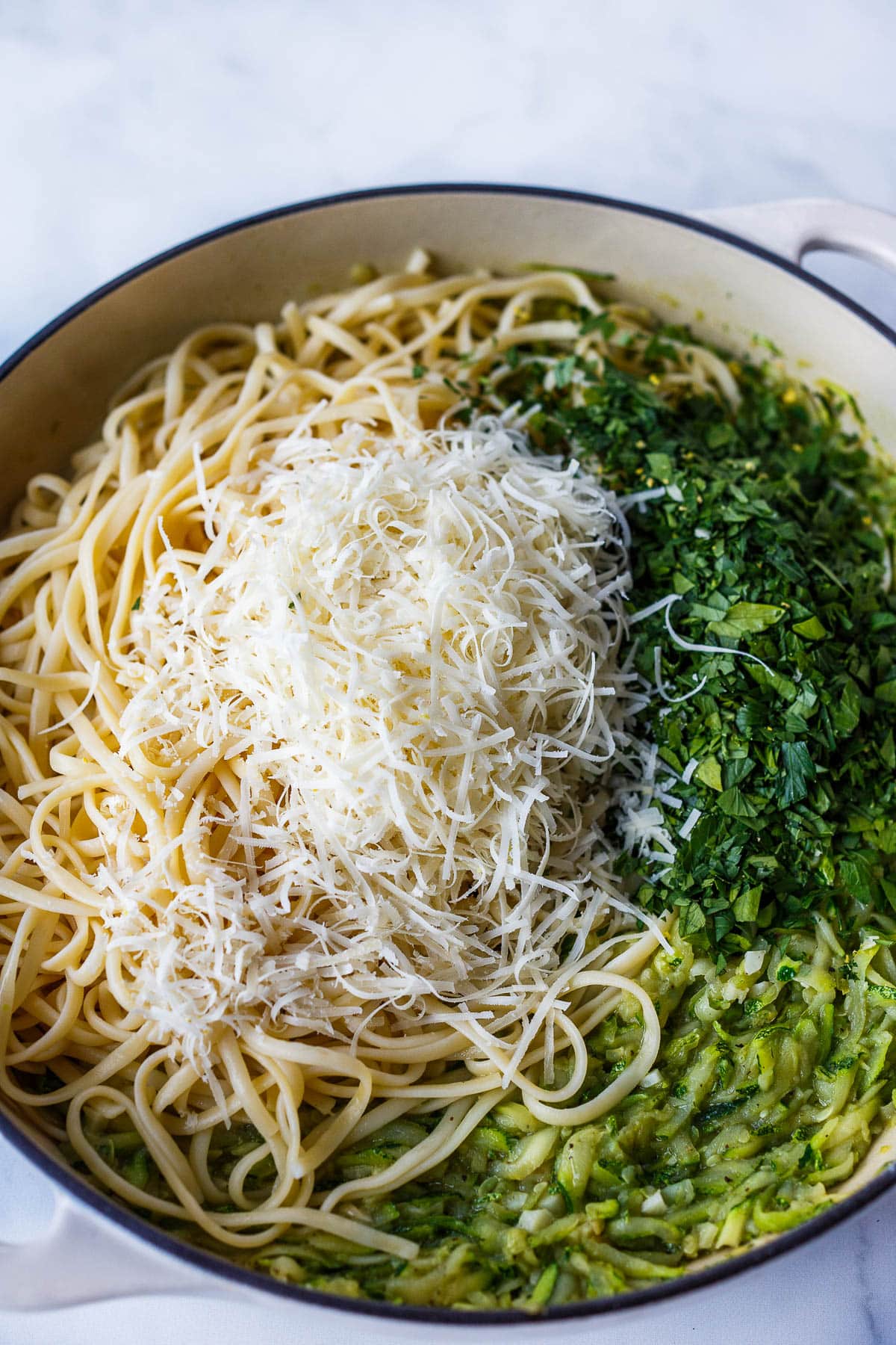Tossing pasta, parmesan cheese, parsley and zucchini sauce.