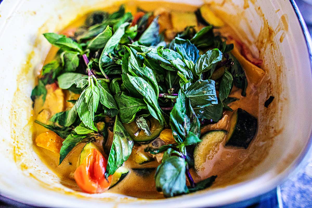 basil added to a pot of zucchini curry