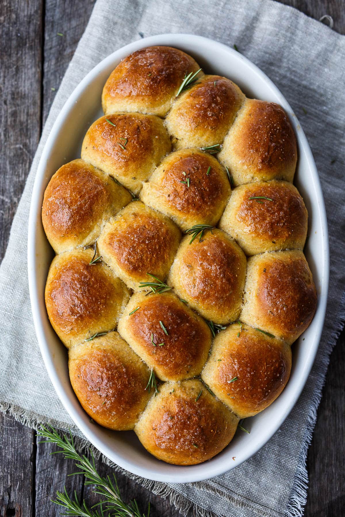 butternut squash dinner rolls in oval baking dish with fresh rosemary scattered over top.