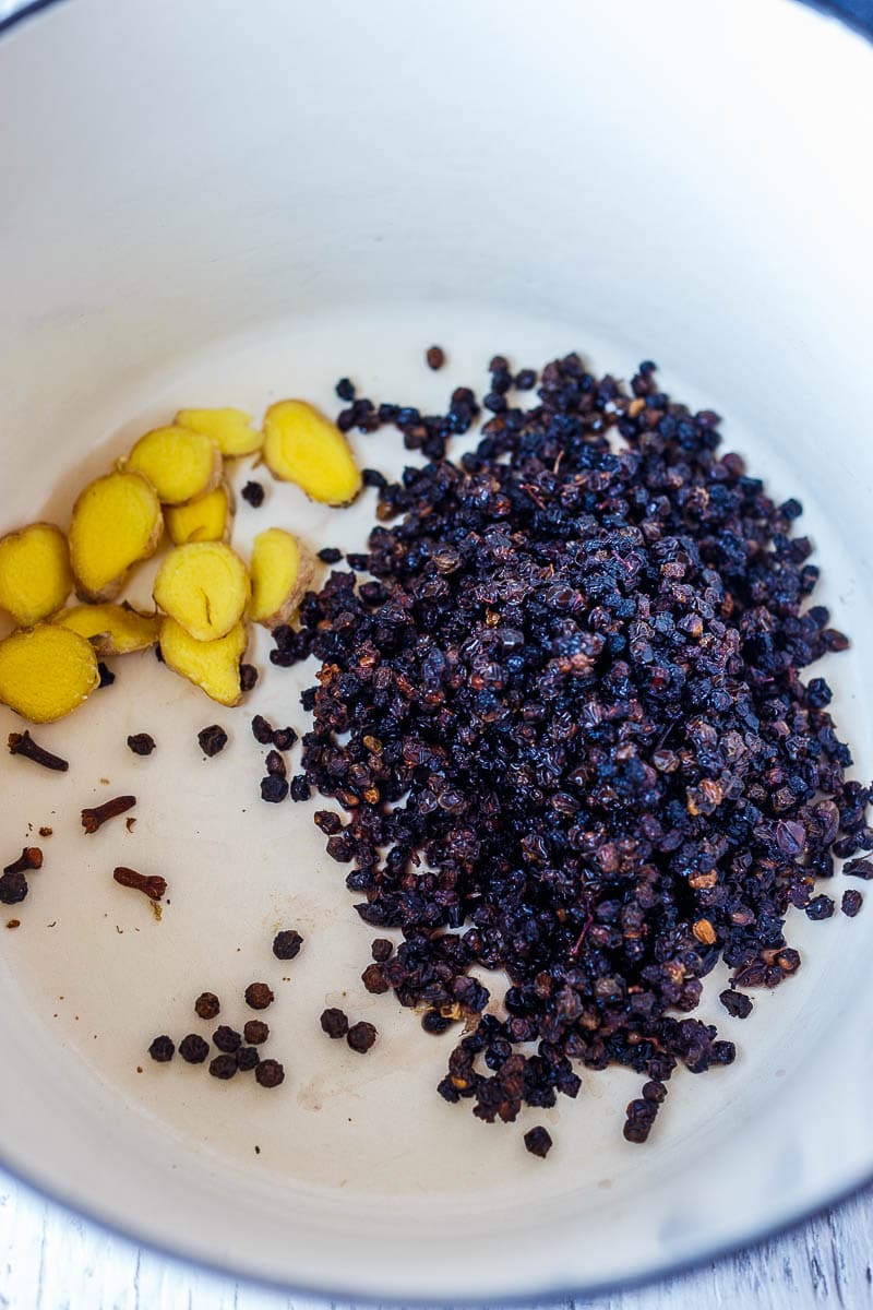 In a white ceramic pot, sliced ginger, dried elderberries, cloves and pepper corns.