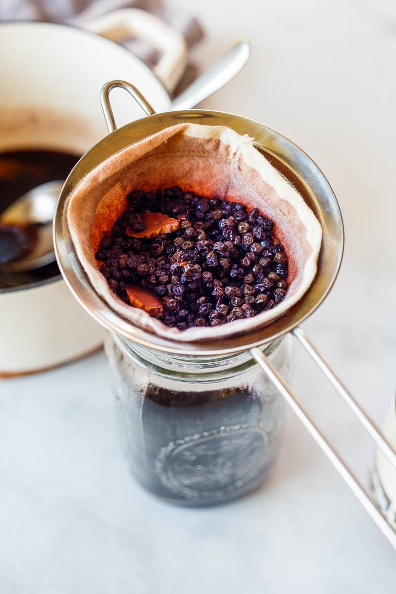 simmered elderberries in cheesecloth over strainer, dripping syrup into mason jar.