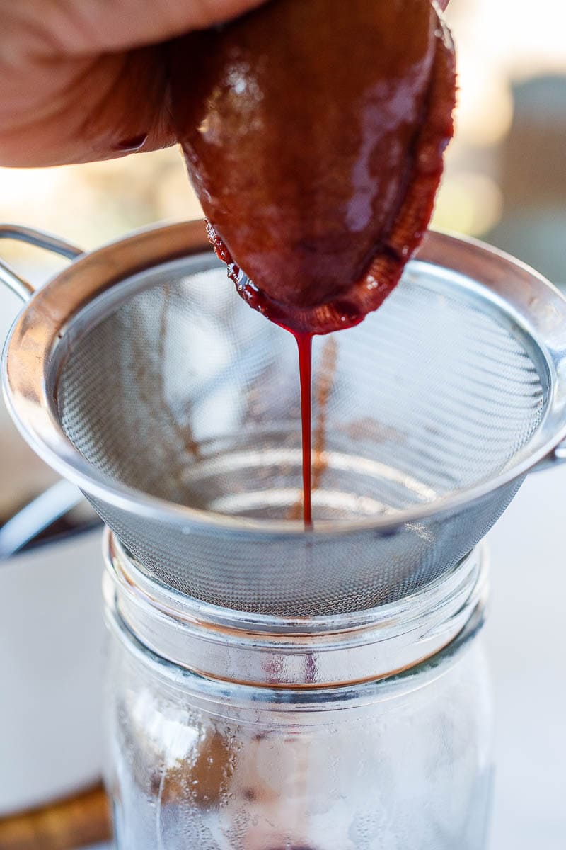 Squeezing juice of elderberries out of cheese cloth and into a mesh strainer.