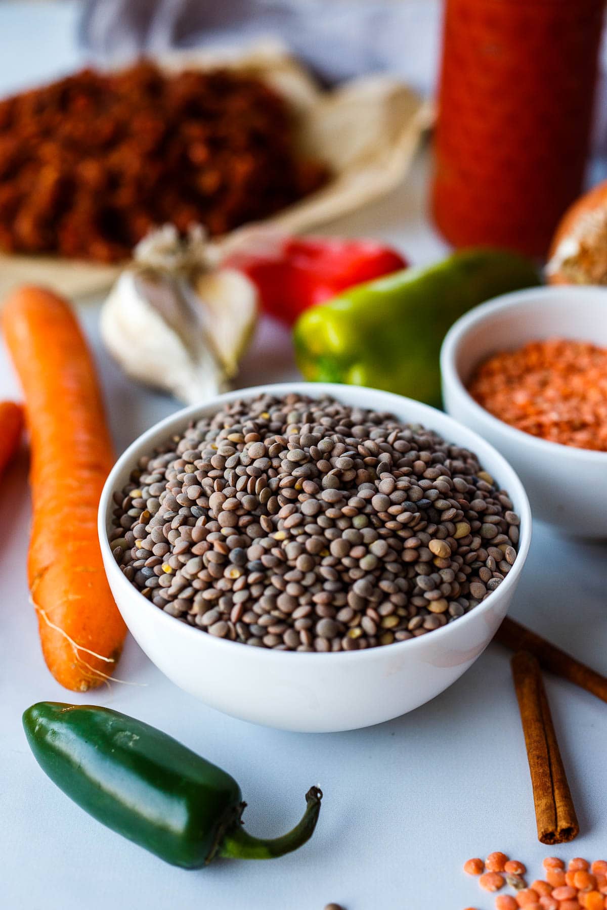 Lentils in a white bowl surrounded by ingredients for chili.