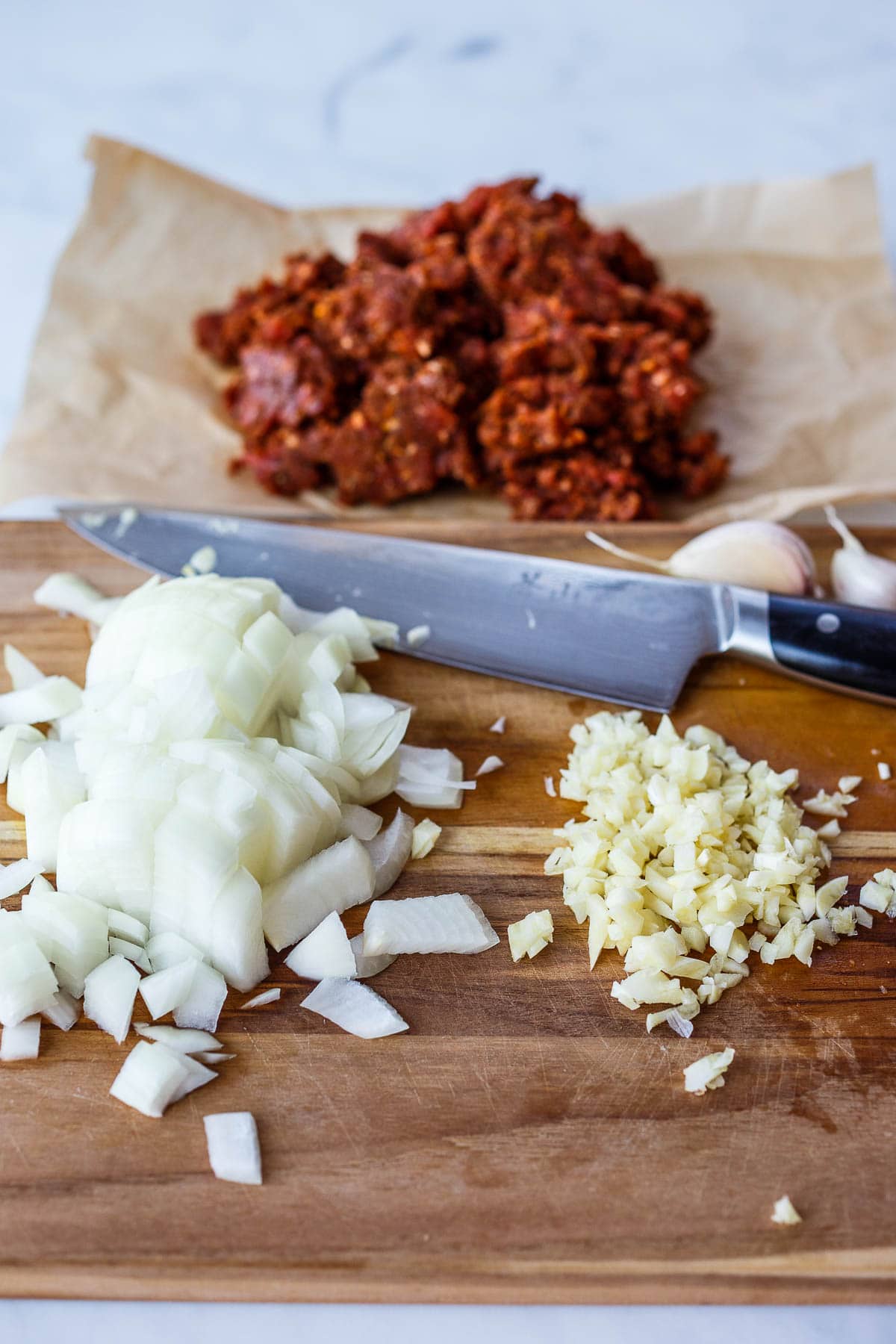Diced onions and garlic on a cutting board with chorizo in the back ground.