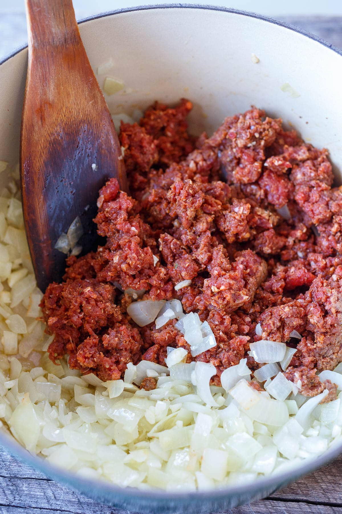 Sautéing chorizo and onions in a ceramic pot with a wooden spoon.