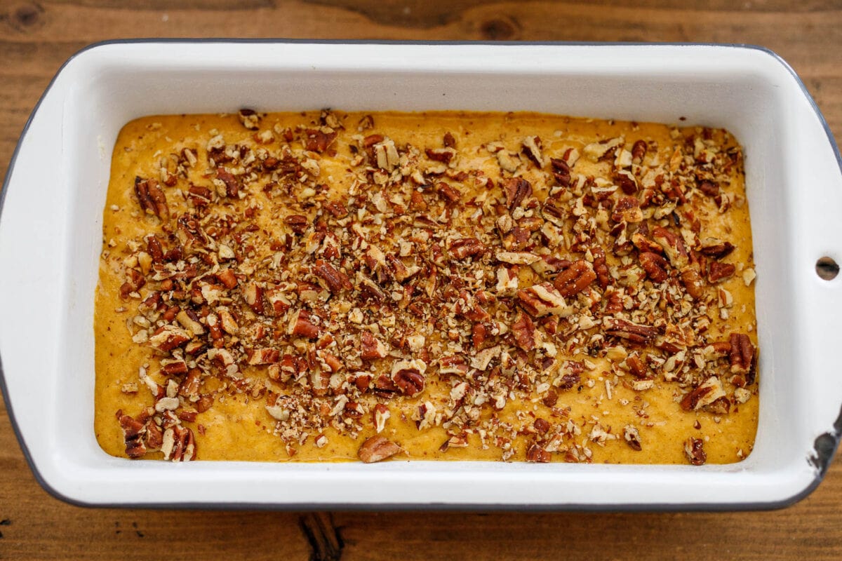 Pumpkin bread batter in a loaf pan with nuts on top.