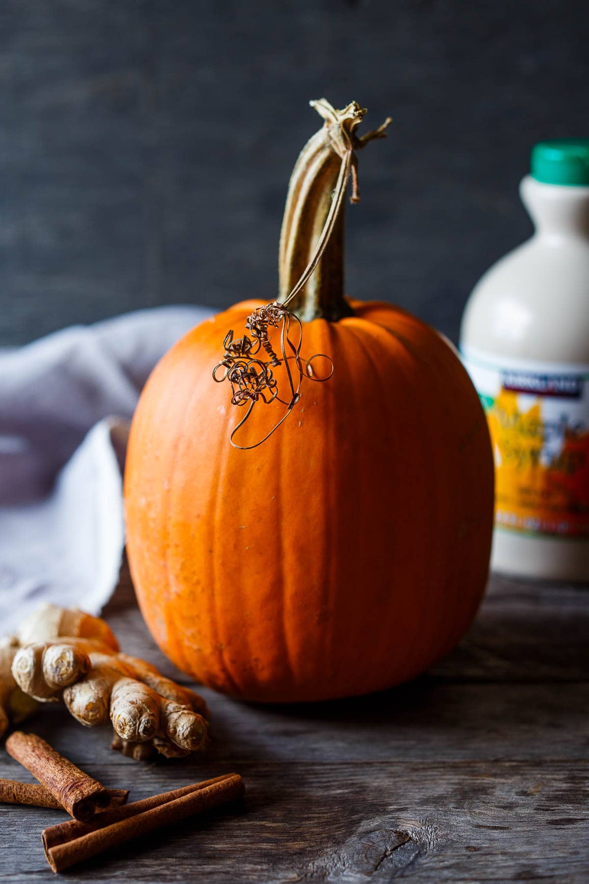 Pie pumpkin with cinnamon sticks and nutmeg on a washed wooden surface.