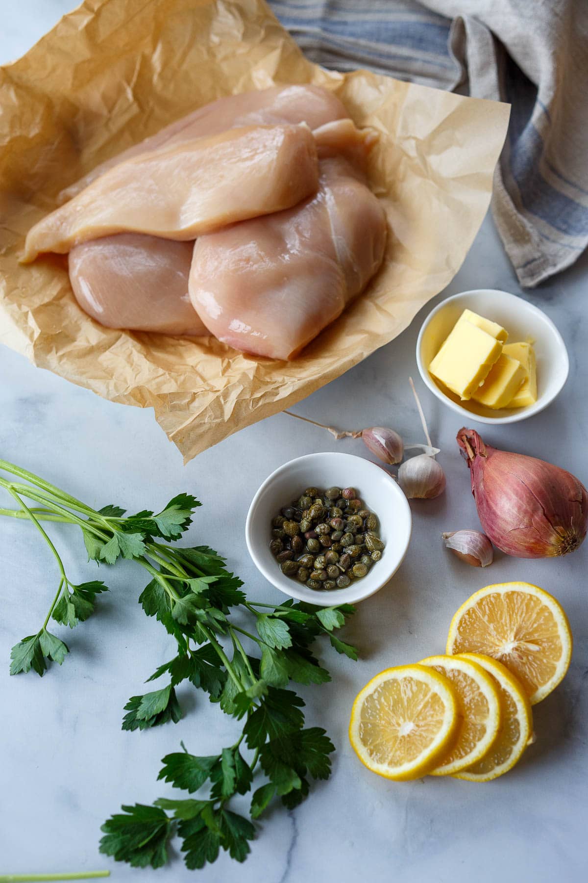 All ingredients for making chicken piccata.  Chicken, butter, capers, garlic, shallot, lemon, parsley.