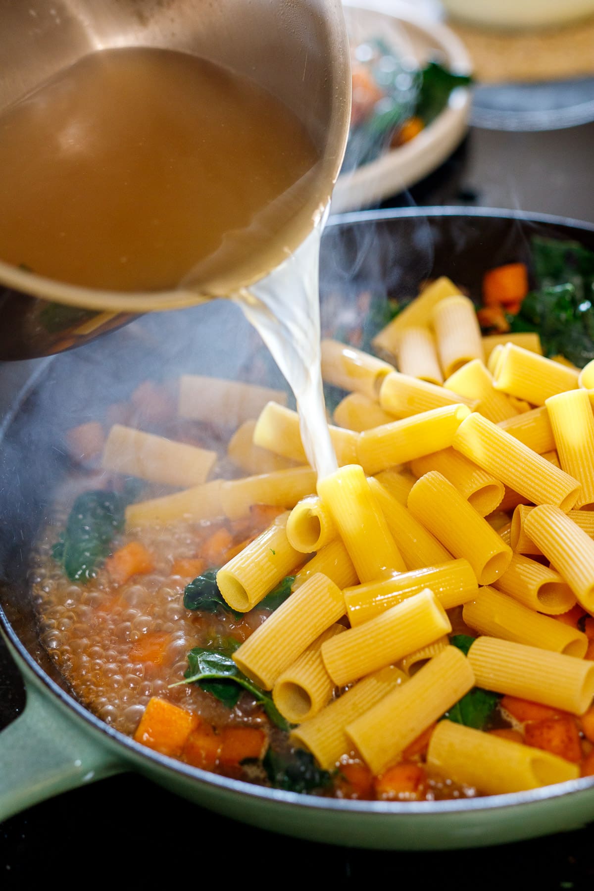 adding broth and pasta to the pan 