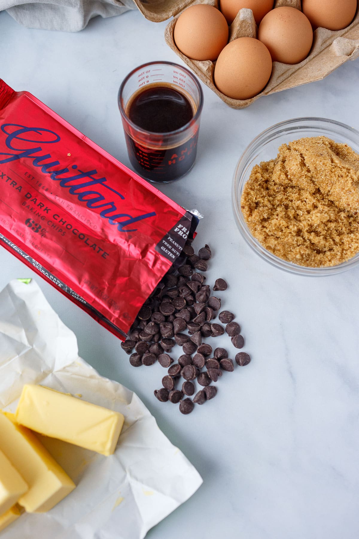 Eggs, coffee, brown sugar, chocolate chips, and butter shown on a marble surface.