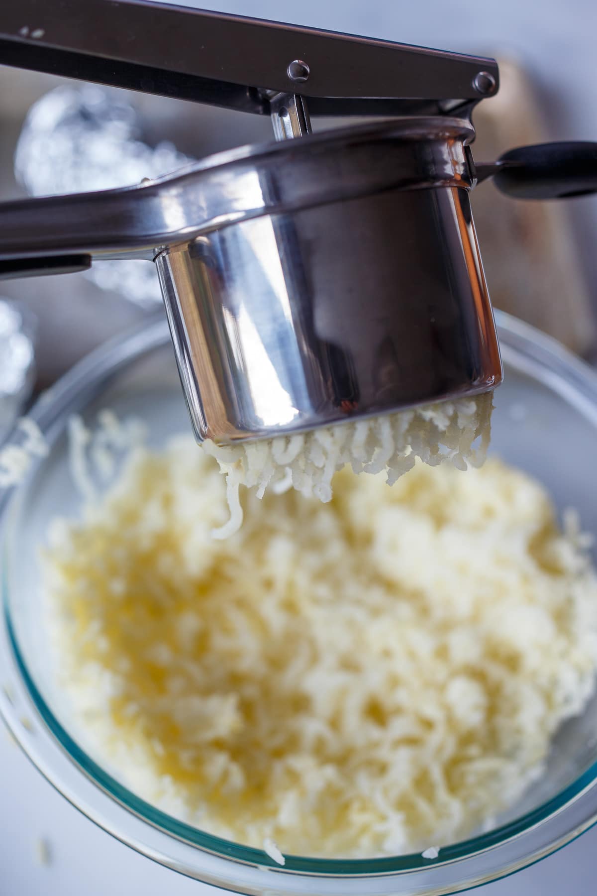 Pressing potatoes through a potato ricer.