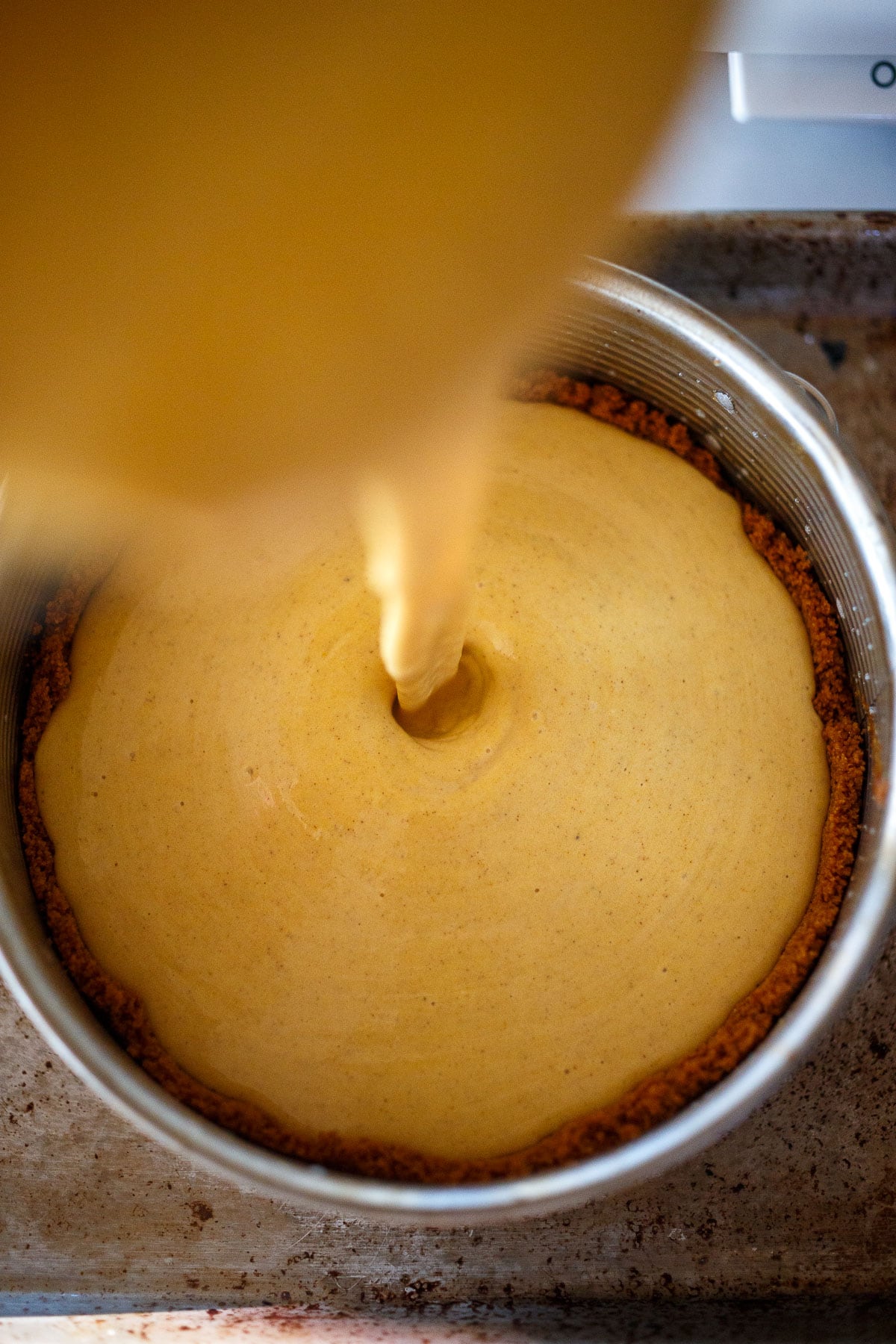 Pouring the pumpkin cheesecake batter into the crust.