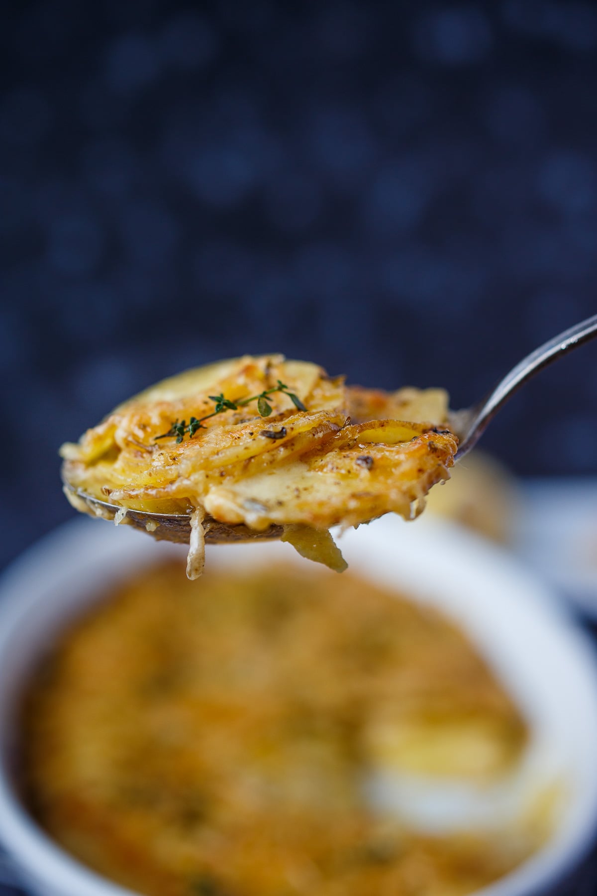 Scalloped Potatoes in a spoon, lifting out of the casserole dish. 