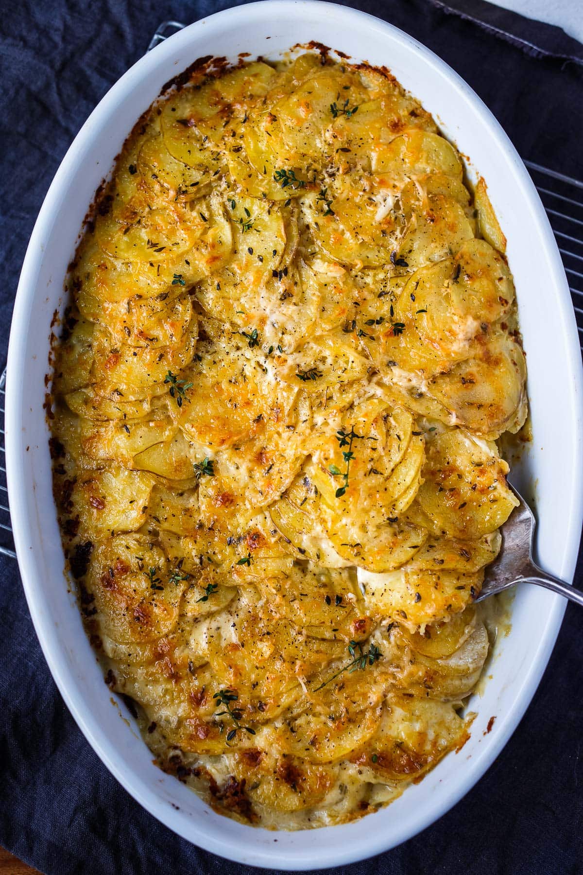 Finished scalloped potatoes in an oval baking dish with a spoon. 