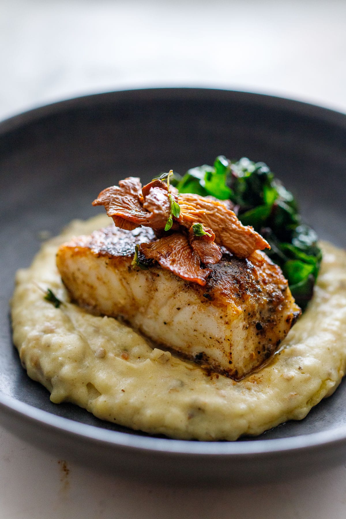 Mushroom dusted halibut topped with sauteed mushrooms over sunchoke puree with simple sauteed greens in a bowl. 