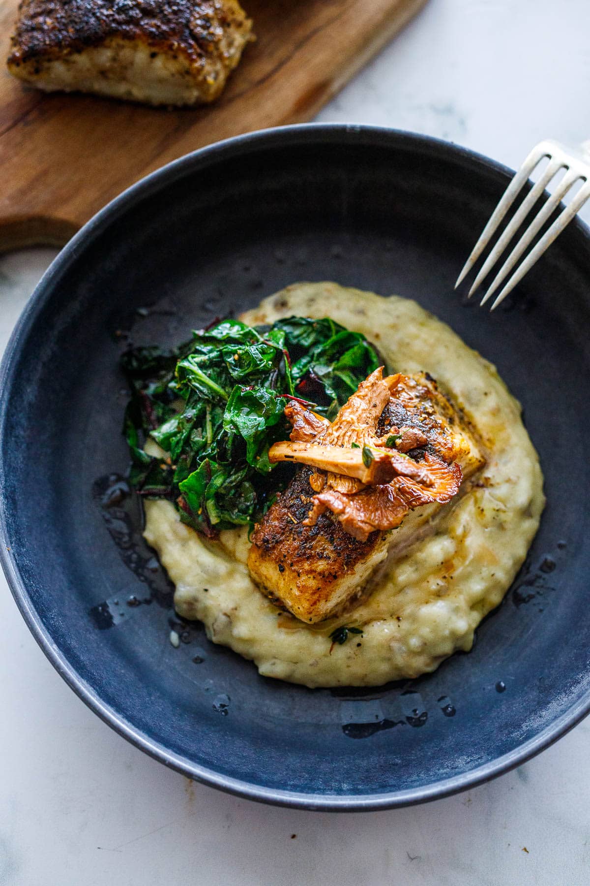 Mushroom dusted halibut in a bowl with sunchoke puree and sauteed greens. 