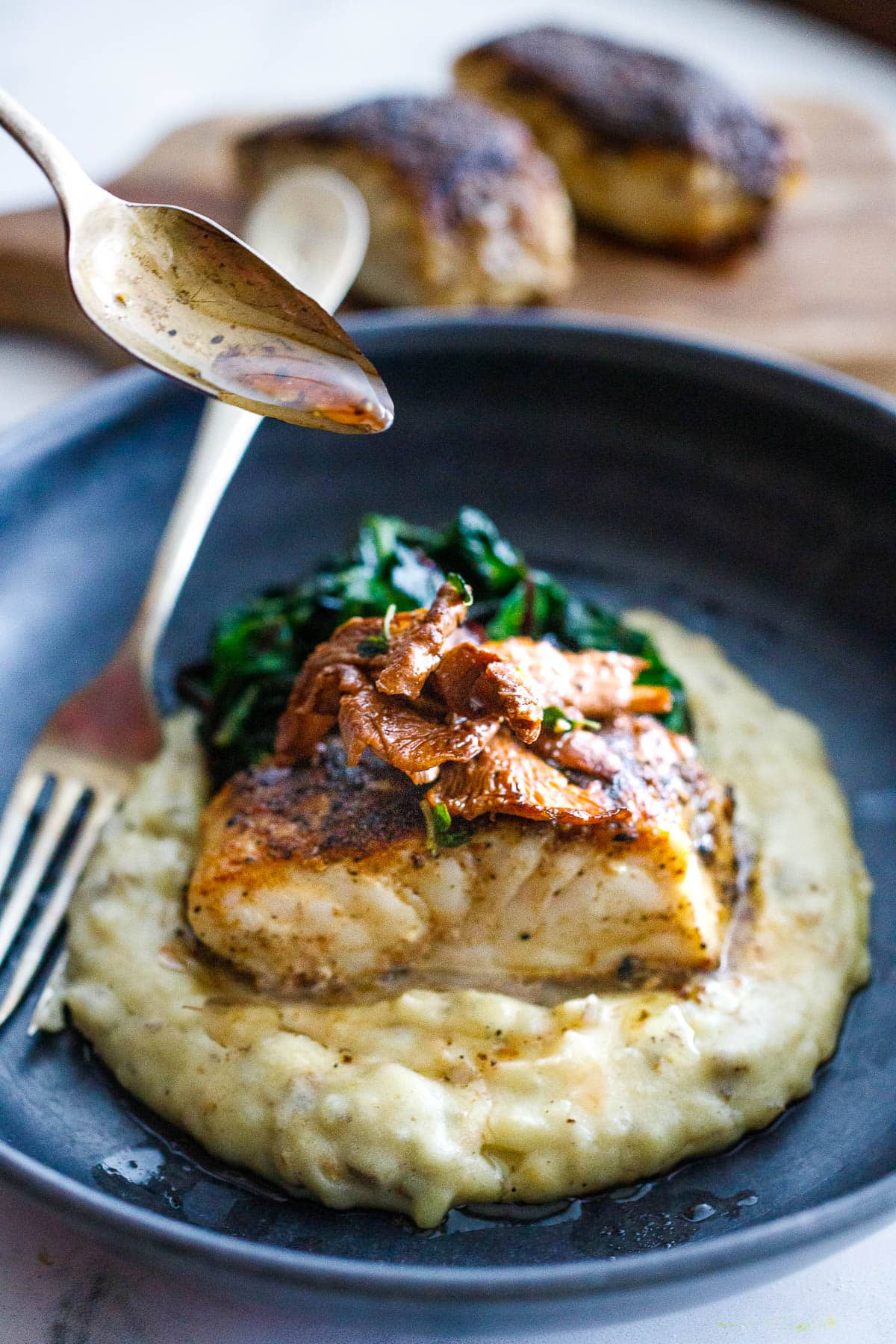 Drizzling a truffle oil vinaigrette over Mushroom Dusted Halibut with sauteed mushrooms, sunchoke puree and  wilted greens, in a bowl with a fork.