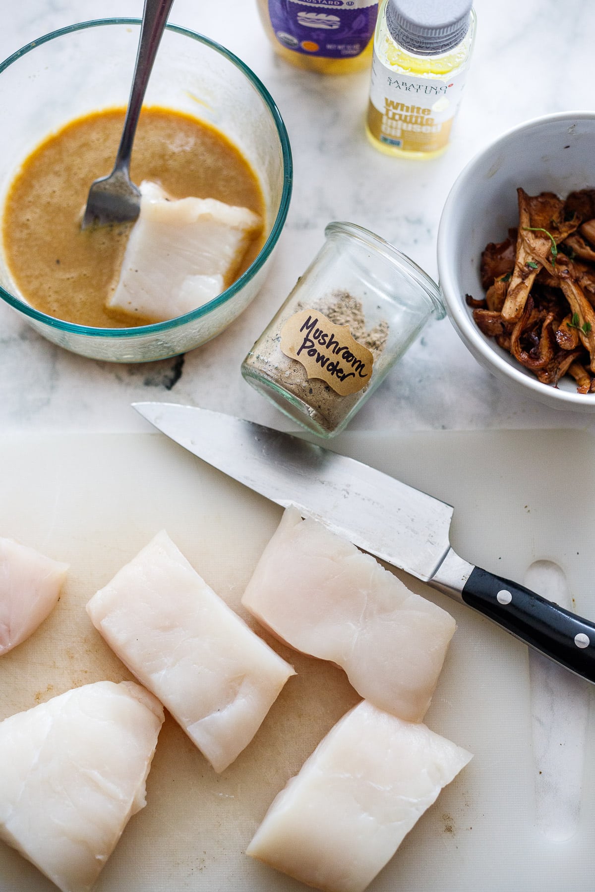 Overview of ingredients- mushroom powder, egg batter, halibut being cut 
 and mushrooms. 