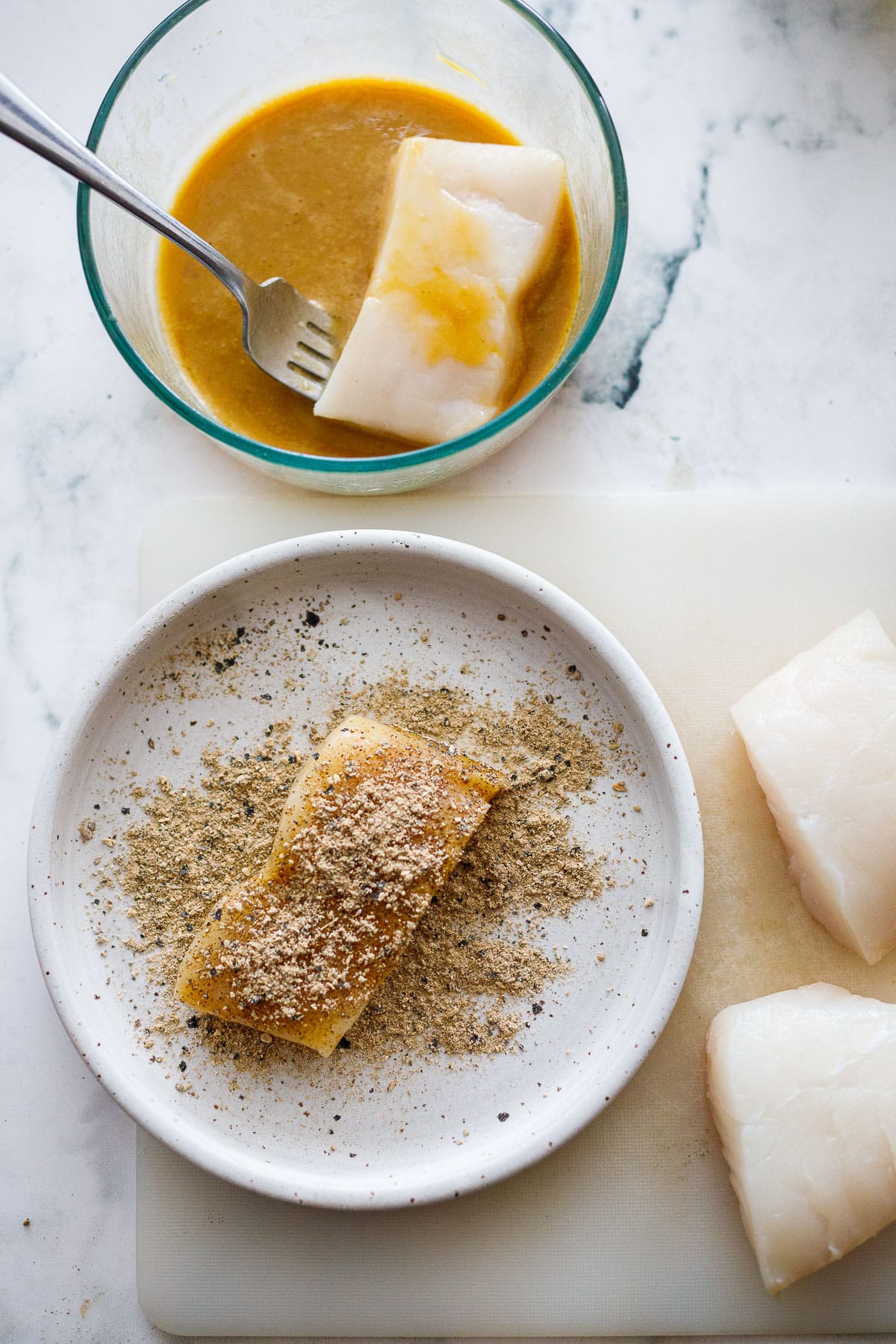 halibut being dipped in the egg batter, then coated with mushroom powder. 