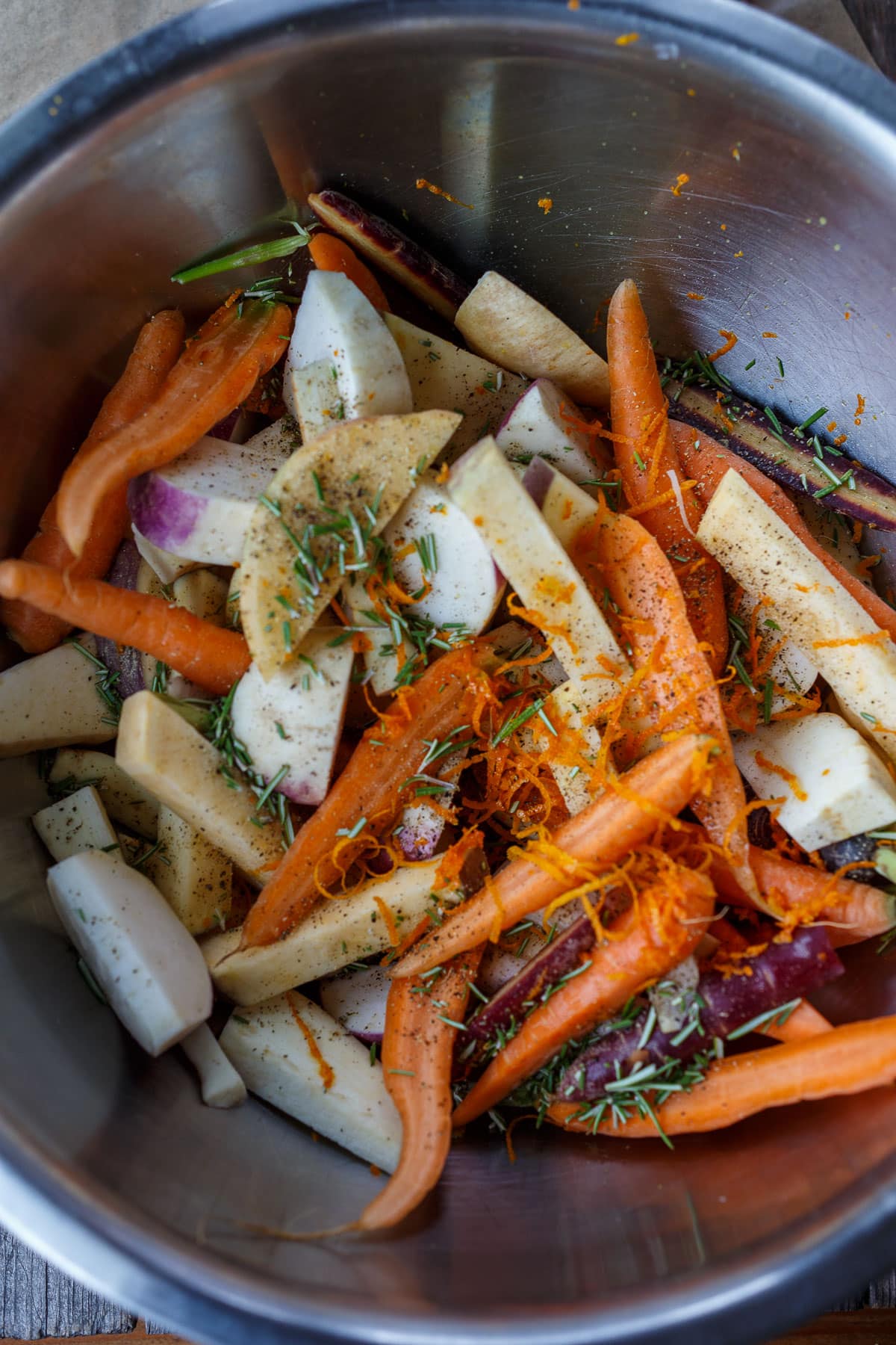 Sliced root vegetables in a bowl with orange zest and rosemary.