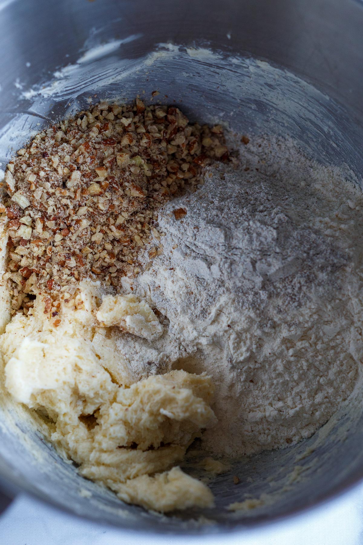 Adding flour and pecans into the mixer with the butter and sugar.