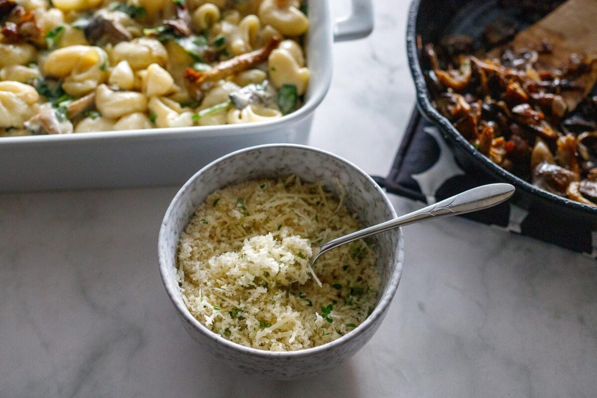 Mac and cheese in a baking dish with a bowl of pecorino, thyme and panko mixed.