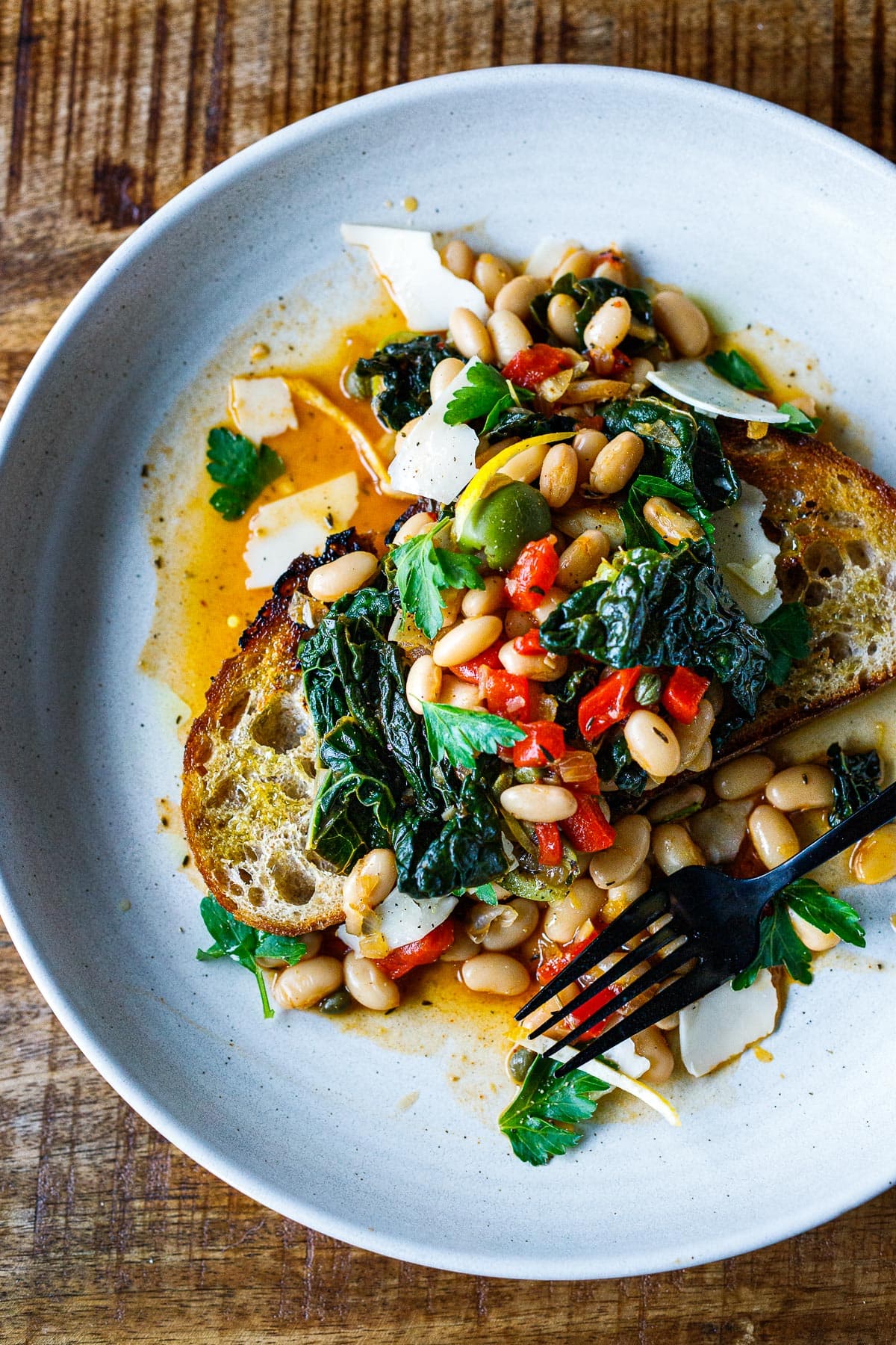 Flavorful Brothy Beans with Lacinato kale, roasted peppers, olives, capers and lemon zest served over crispy garlic-infused sourdough toast.