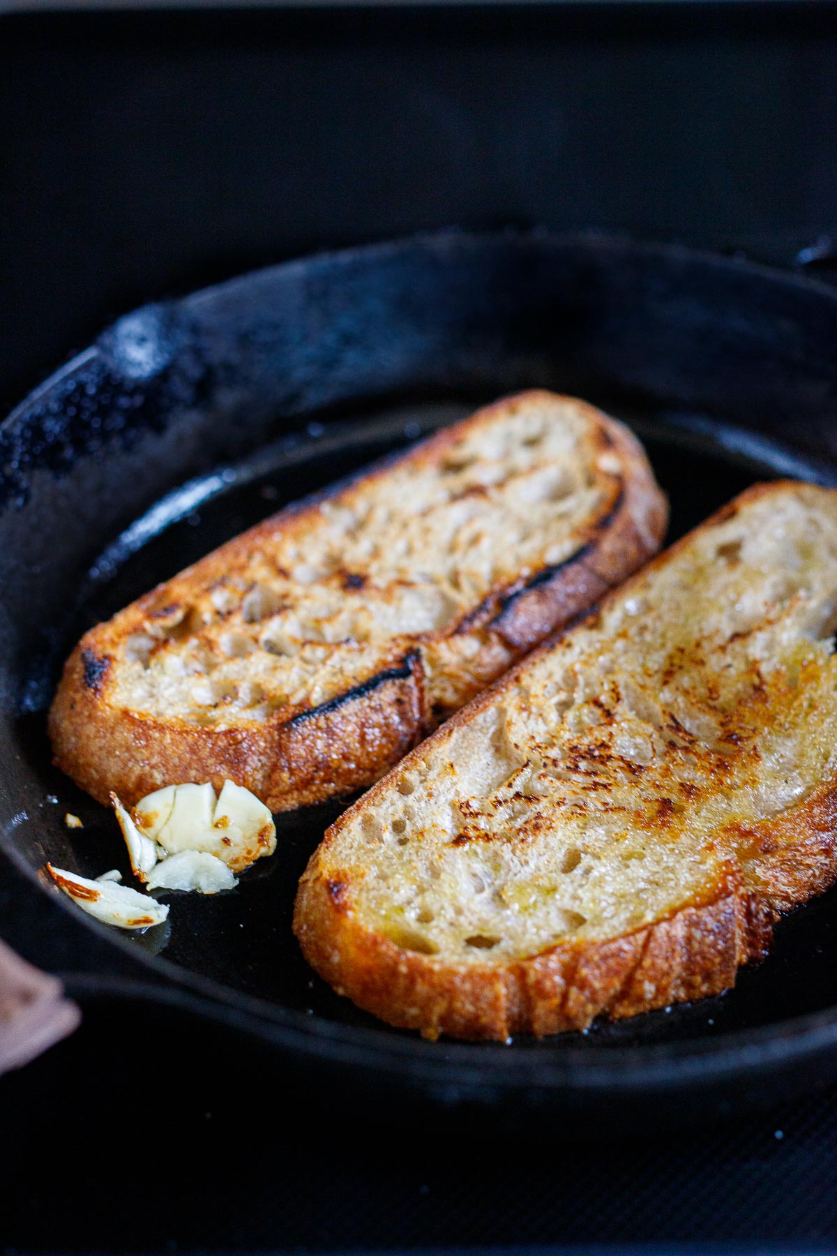 2 pieces of toast in a skillet with olive oil and smashed garlic clove