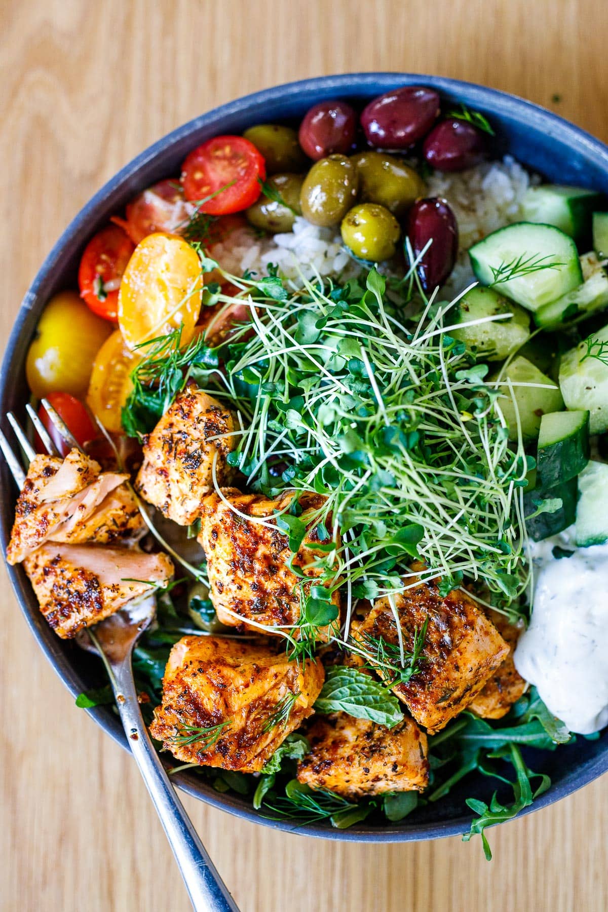 Our 25 BEST Salmon Recipes: Greek Salmon Bowl with rice, greens, olives, tomatoes, cucumber, tzatziki and greek dressing.