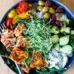 Delicious and healthy Greek Salmon Bowl with rice, greens, olives, tomatoes, cucumber, tzatziki and greek dressing.