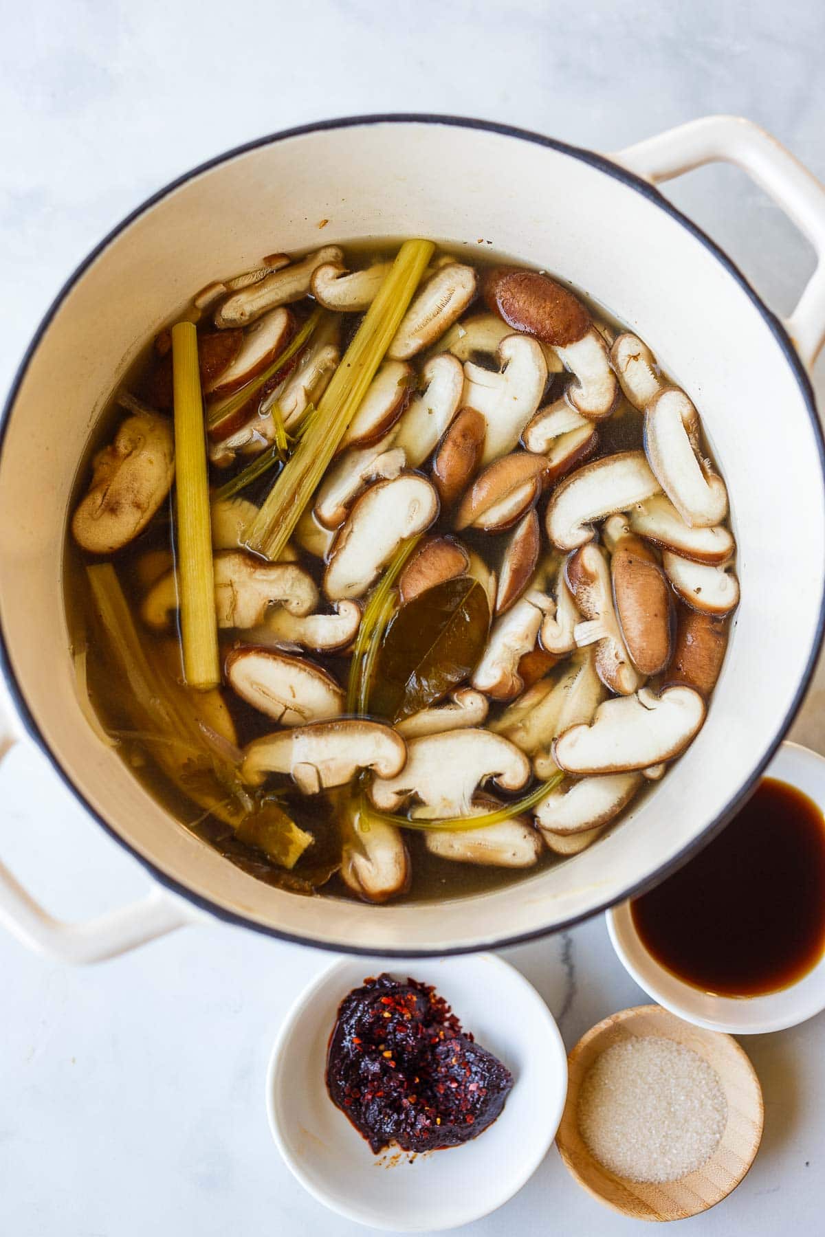 Simmering tom yum soup broth ingredients in a pot with mushrooms.