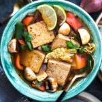Tofu tom yum soup with vegetables in green bowl with a spoon