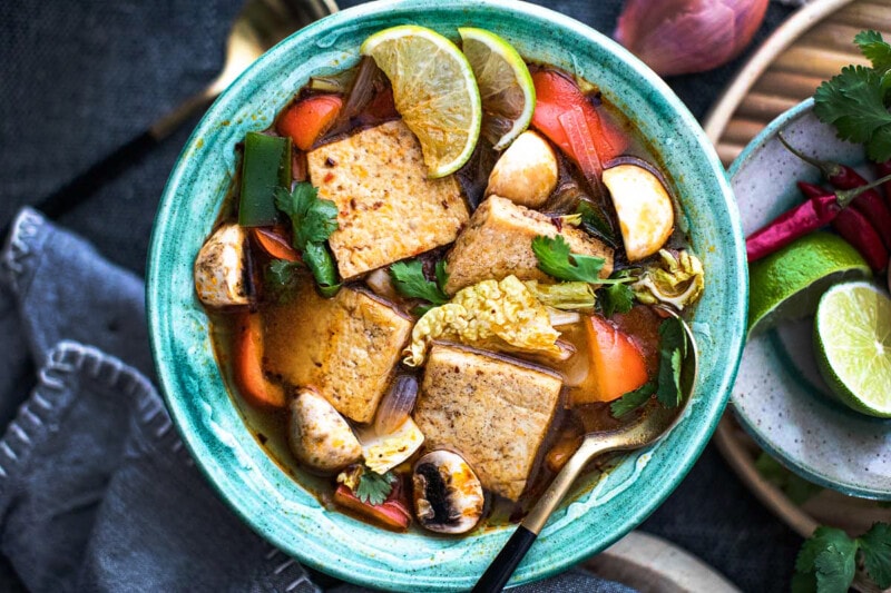 Tofu tom yum soup with vegetables in green bowl with a spoon