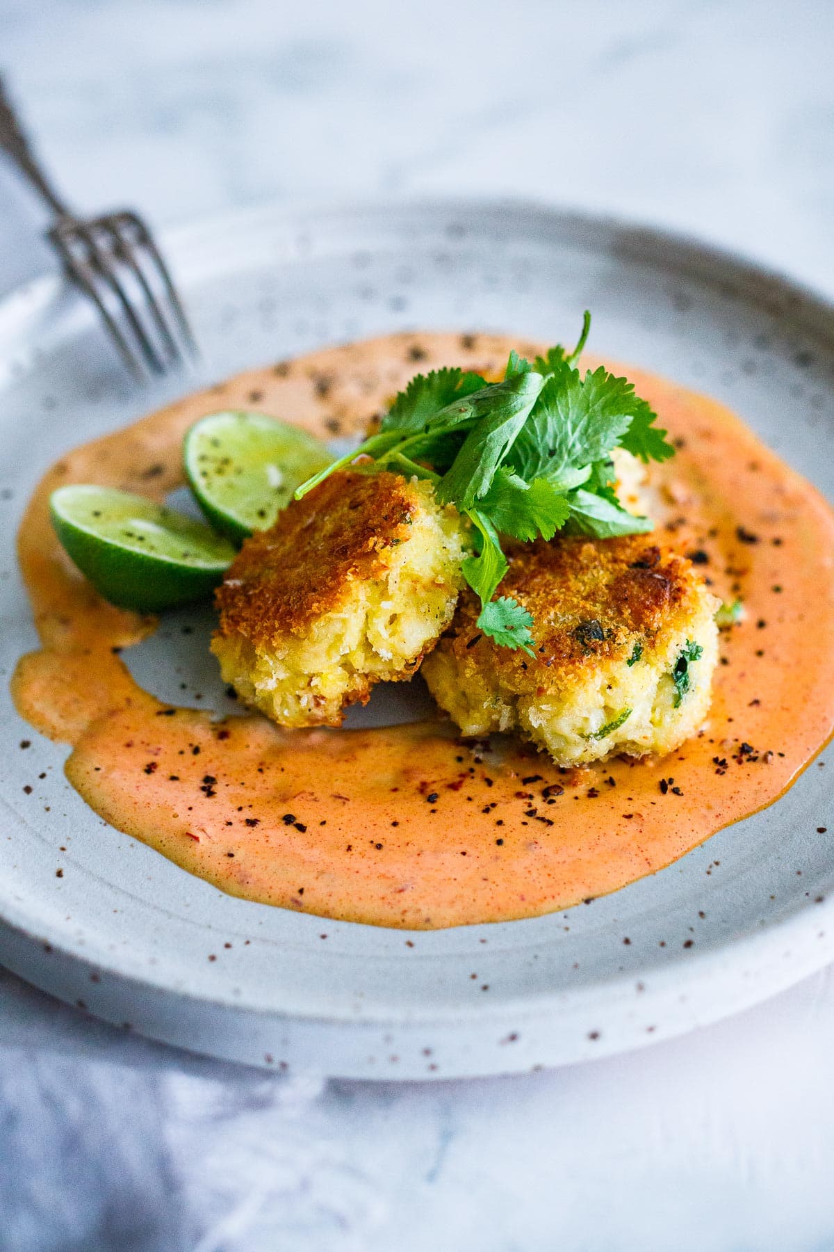 Dungeness Crab Cakes over a Red Pepper Vinaigrette on a white plate. 