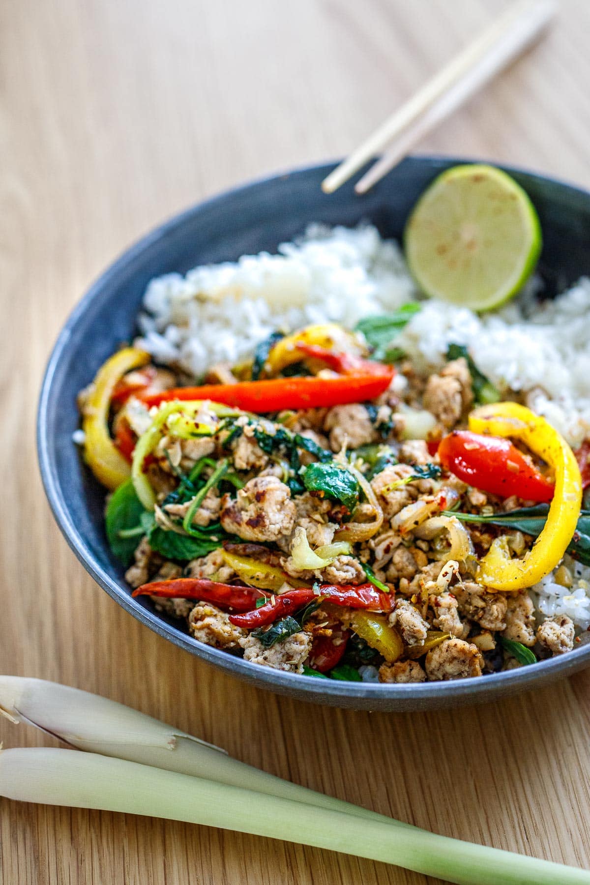 A bowl of rice covered with lemongrass chicken and a lime wedge. 