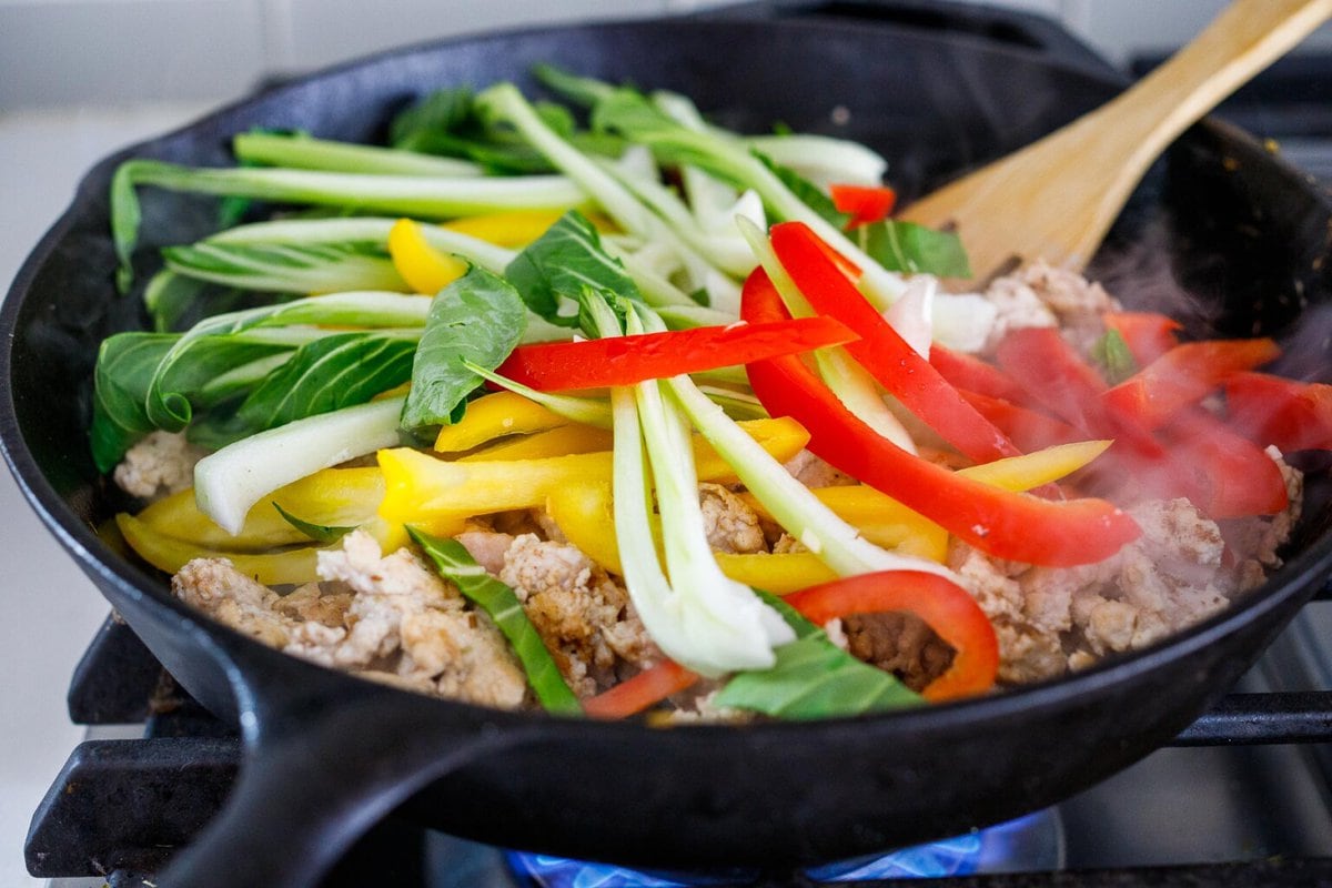 Adding veggies to the skillet, over the chicken.