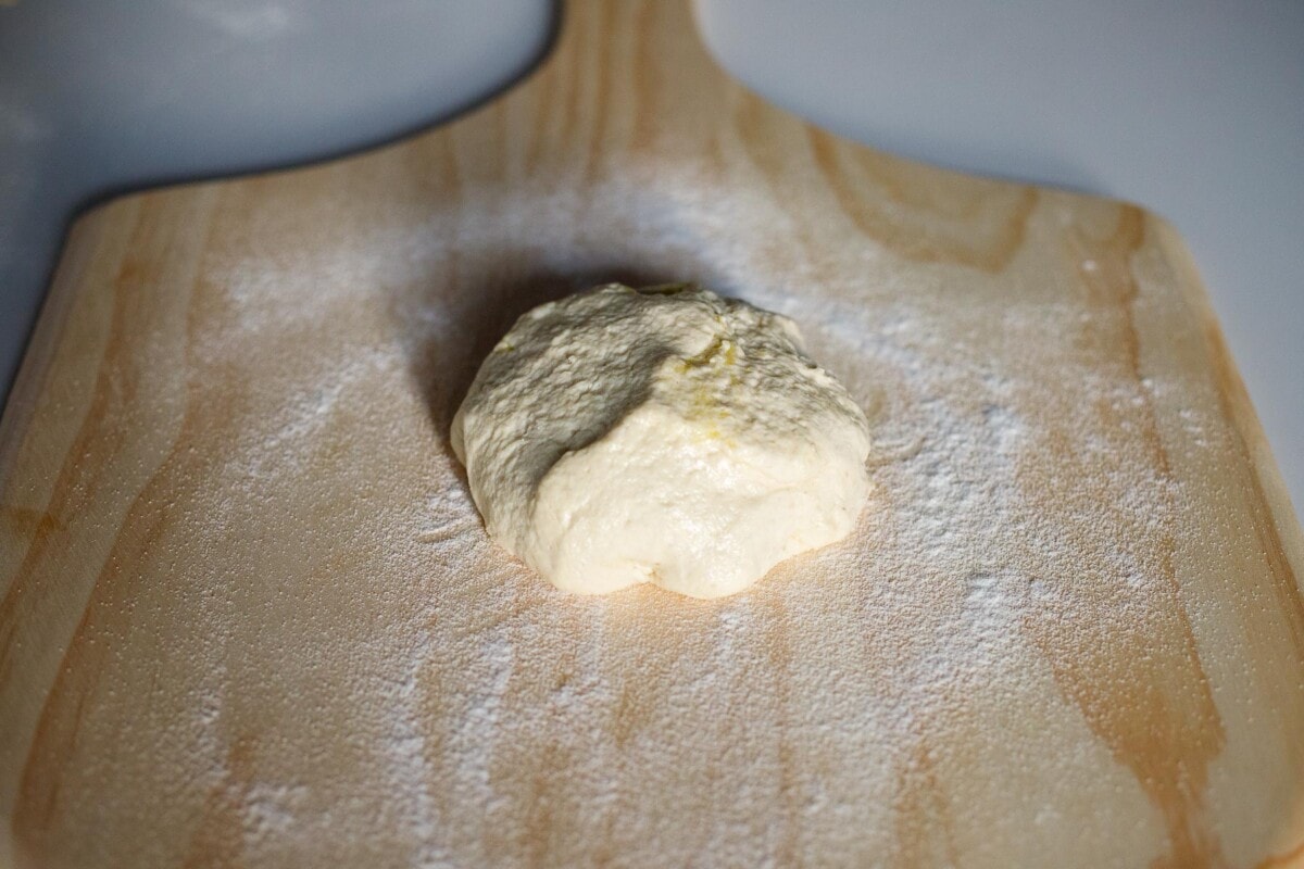 A ball of pizza dough on a floured wood pizza peel. 