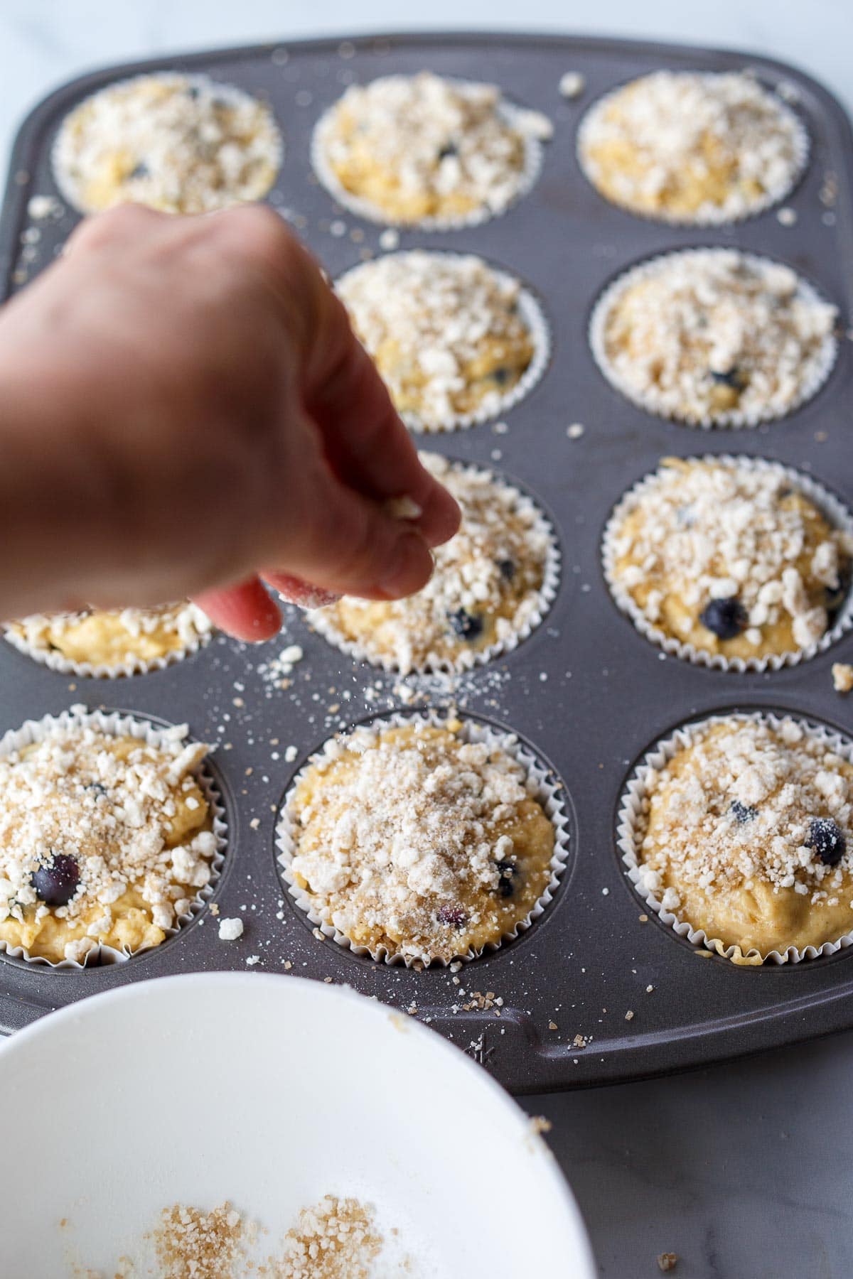 Sprinkling streusel over the muffin batter.