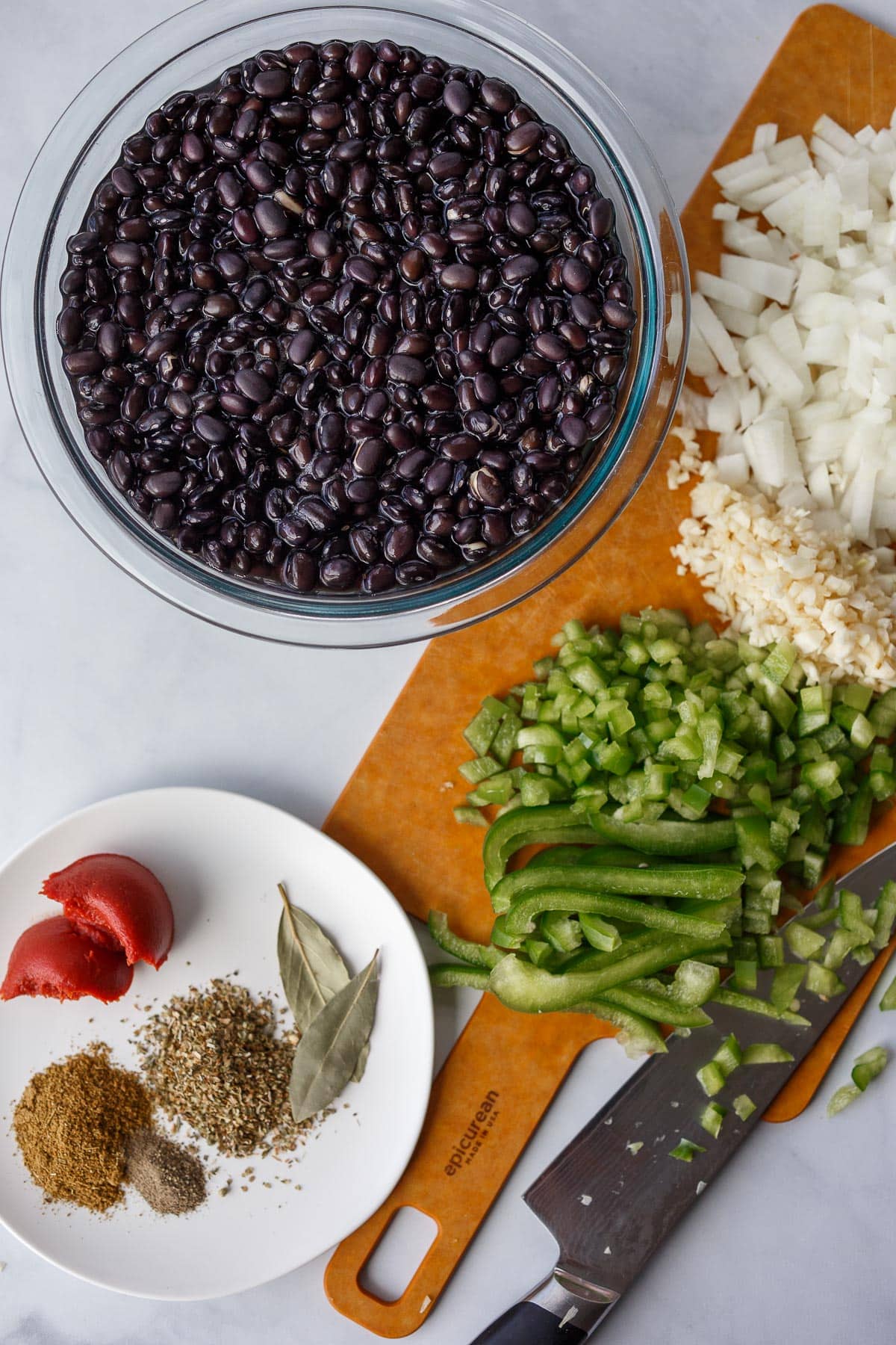 Soaked black beans, chopped peppers and onions on a cutting board, spices measured out.