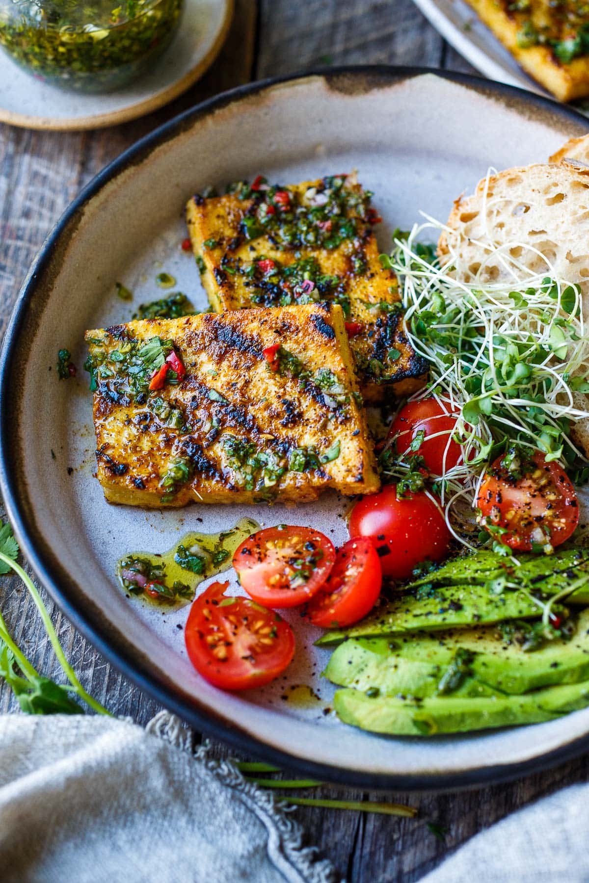 Grilled Tofu served on a plate with tomatoes, avocado, sprouts. 
