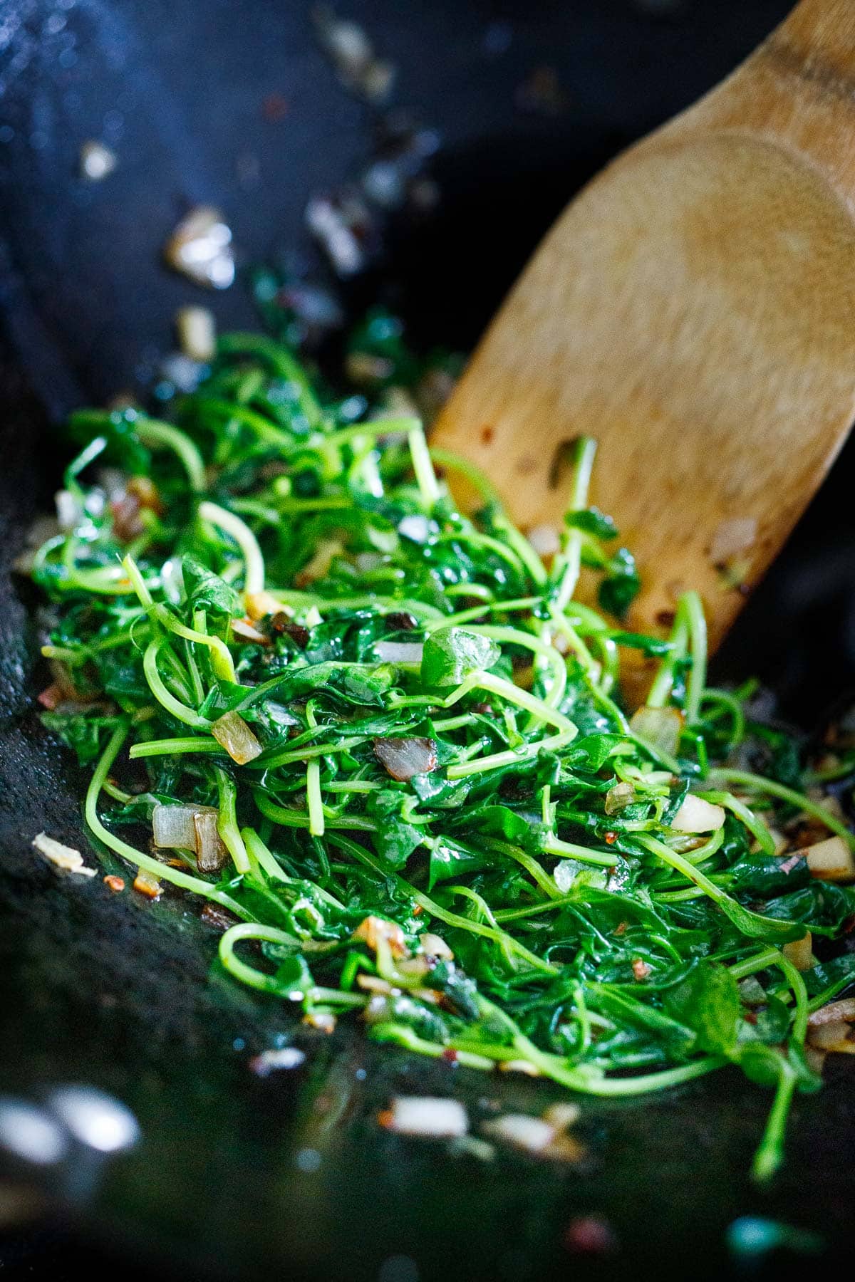 cooked pea shoots in a wok.
