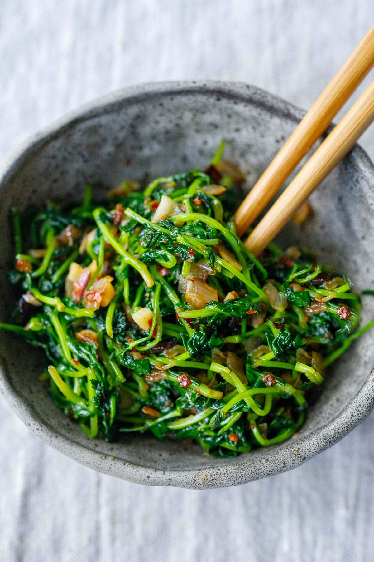 Pea shoots with garlic, shallot and chili flakes in a bowl with hop sticks