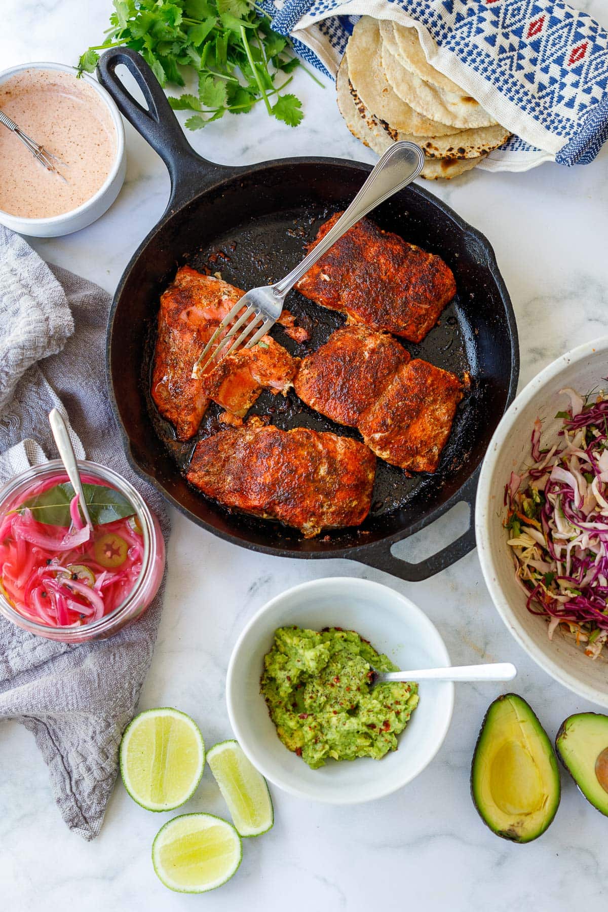 Gathered ingredients to make the tacos: avocado mash, pickled onions, salmon tortillas, taco slaw, taco sauce. 